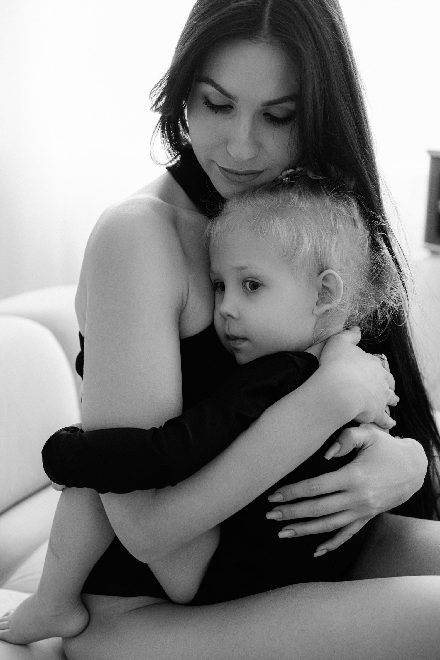 Black and white photo of a dark-haired mother tenderly embracing her young blonde toddler child.