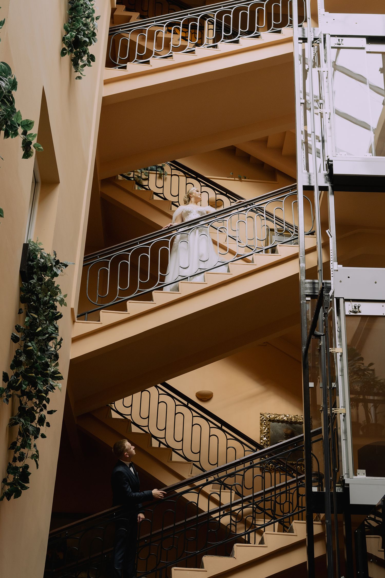 Modern staircase with white metal railings and decorative vines climbing along beige walls in an interior space.