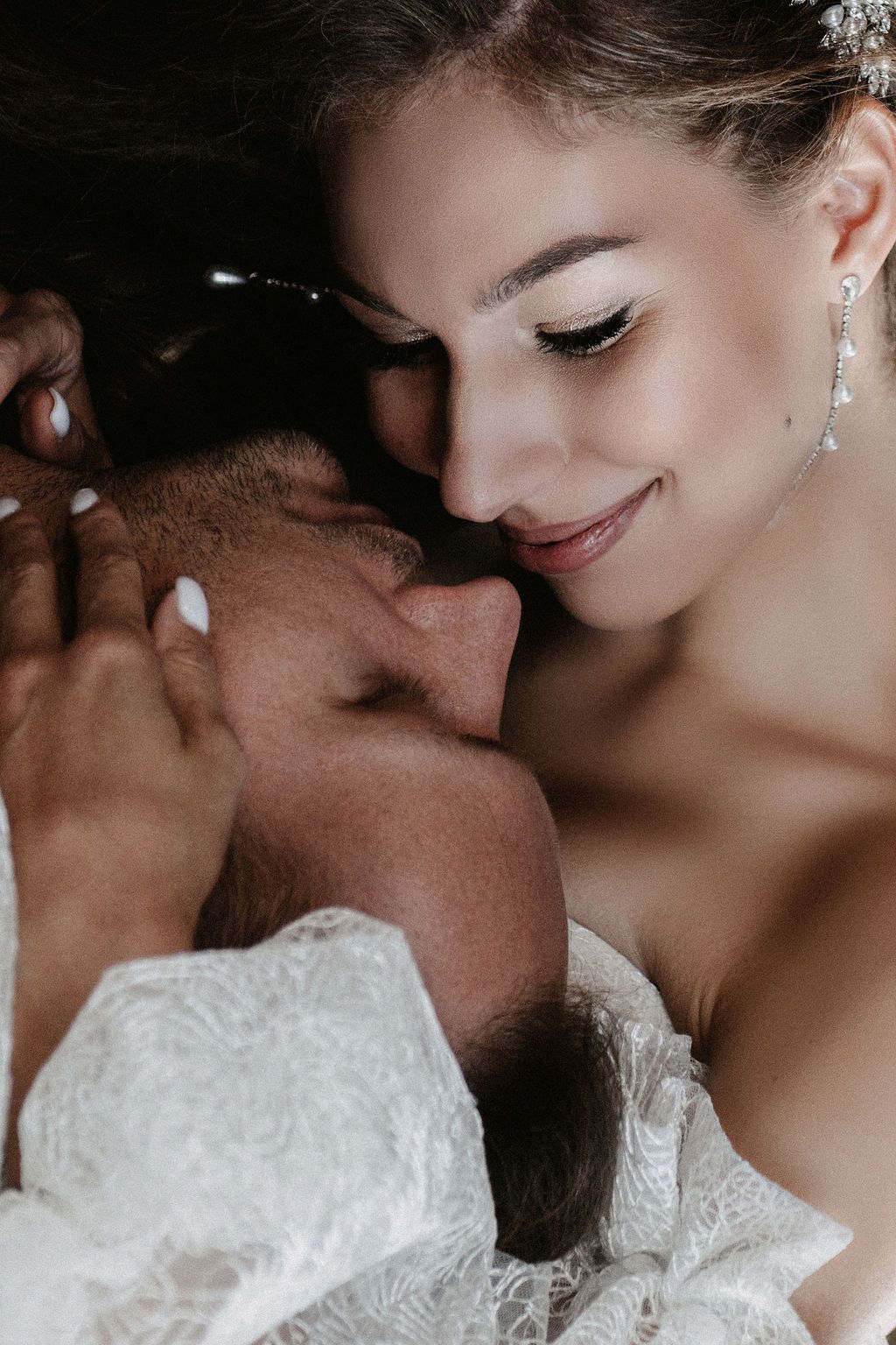 Bride in lace dress smiling tenderly at groom during intimate romantic wedding moment.