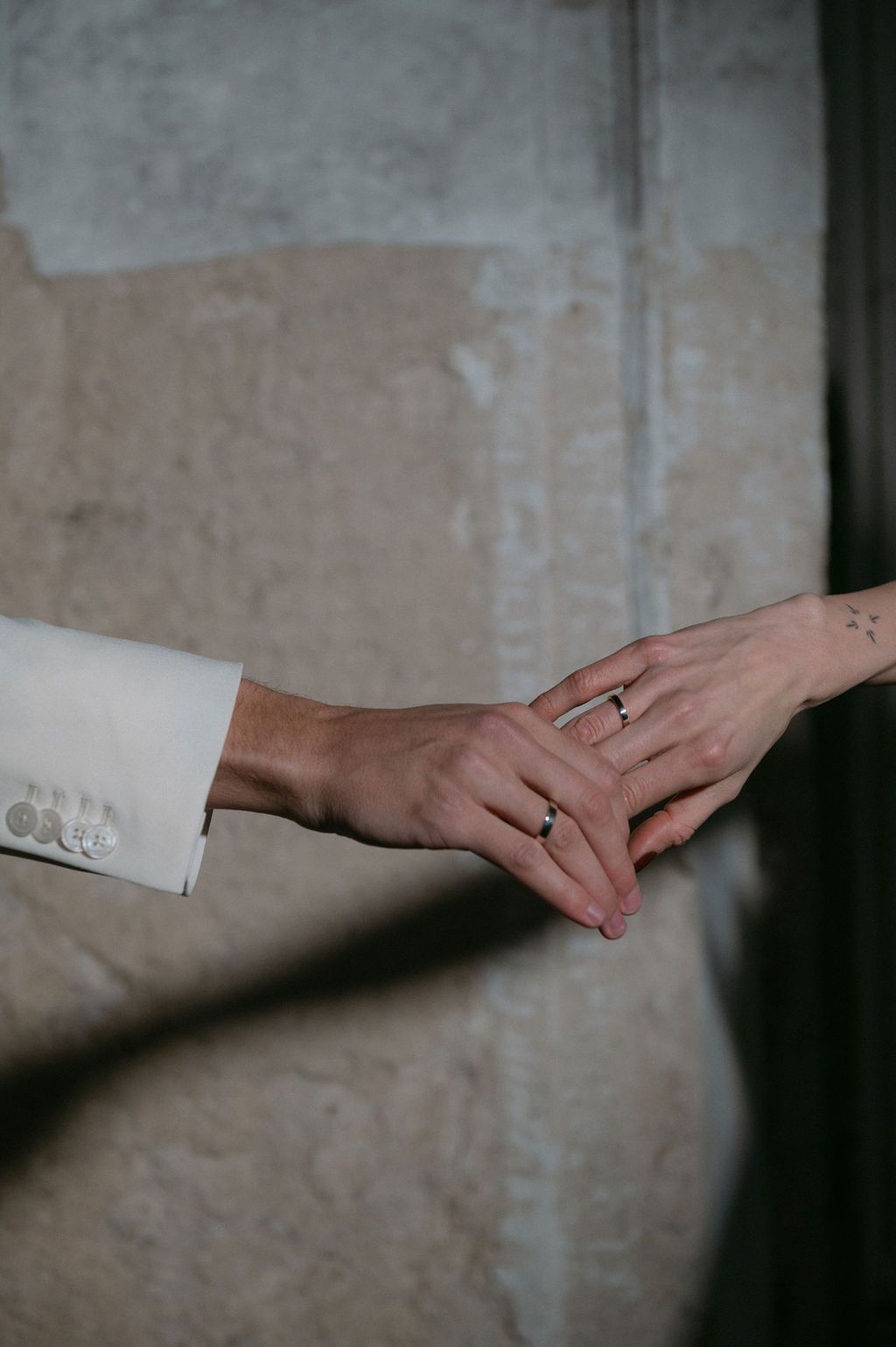 Close-up of newlyweds holding hands, both wearing wedding rings, groom in white suit jacket.