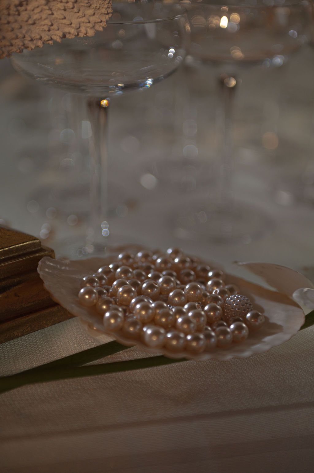Elegant pearl beads displayed in a shell dish beside crystal champagne glasses on a white tablecloth.