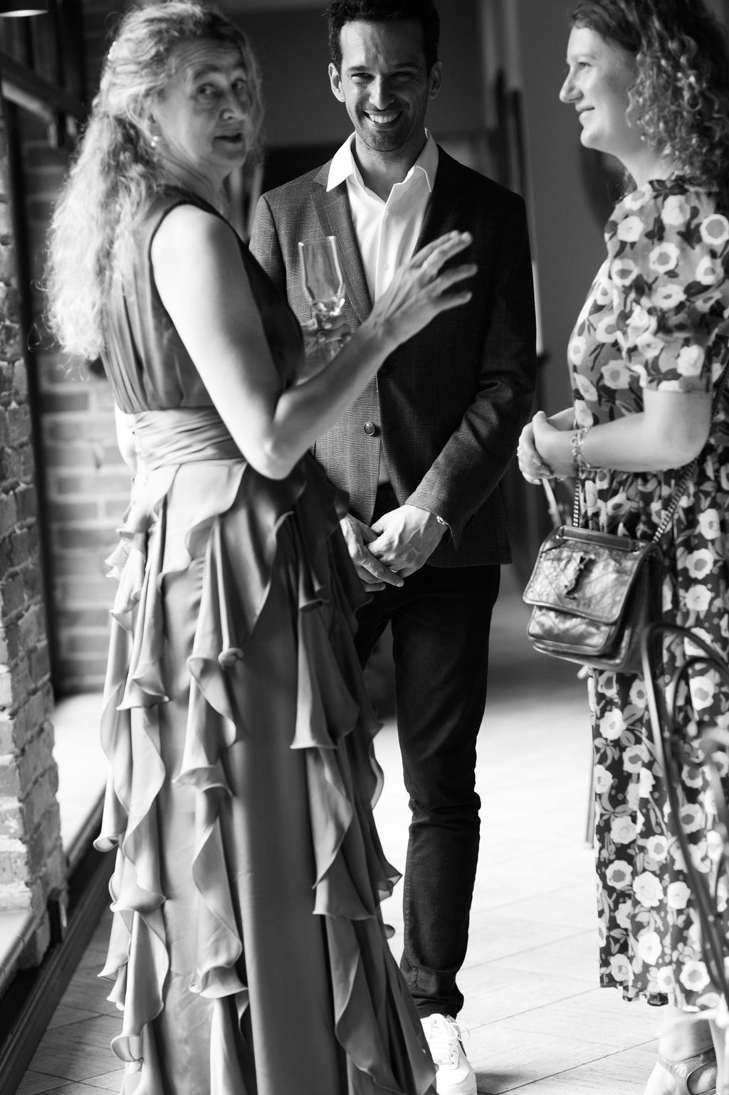 Black and white photo of three elegantly dressed guests socializing at an indoor wedding reception event.
