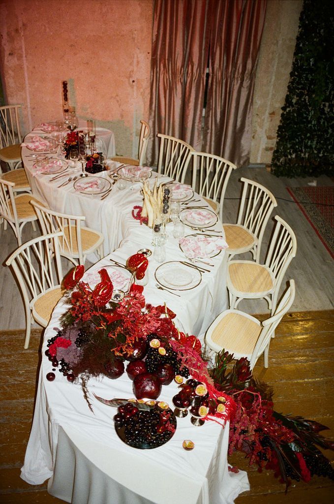 Elegant banquet table with white linen, red floral arrangements, and place settings in a rustic venue.