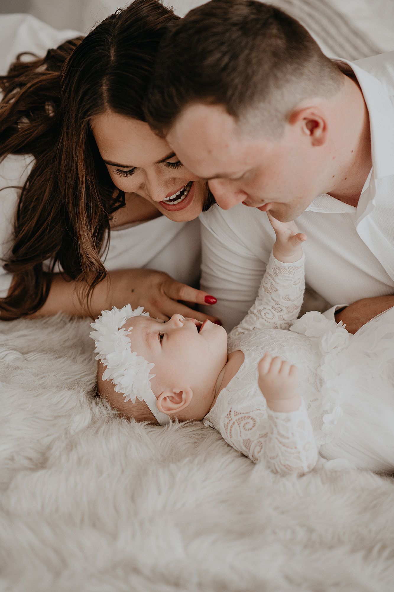 A tender moment between parents and their baby lying on white bedding, captured in a series of intimate black and white photos.