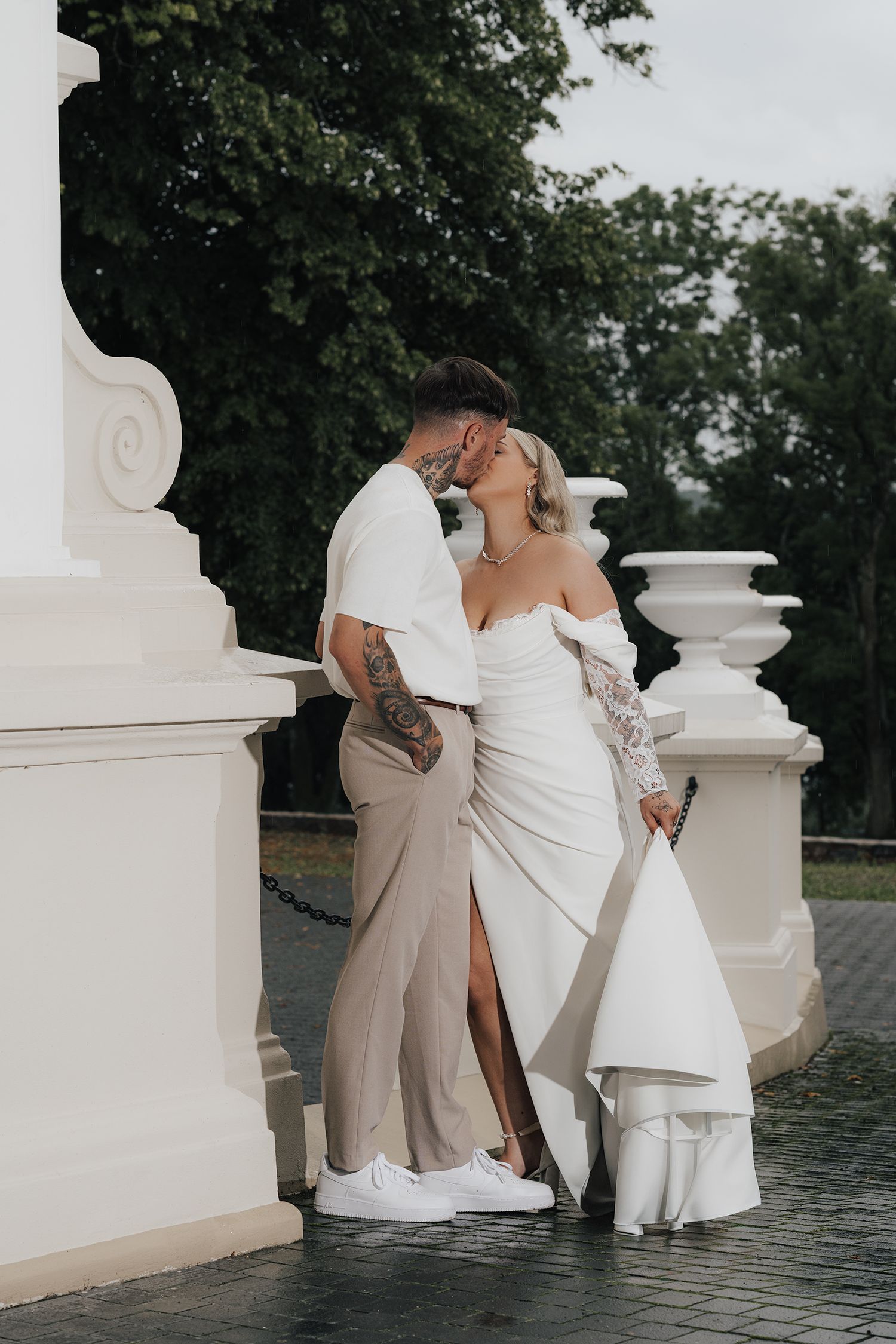 A romantic wedding couple embraces on an elegant white stone terrace with ornate architectural details.