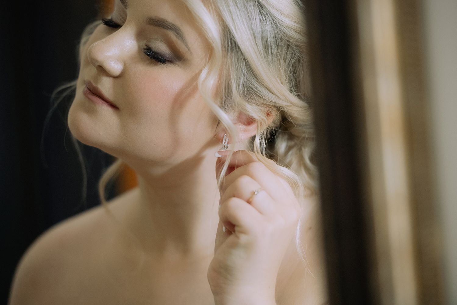 A bride getting ready for her wedding with elegant makeup and hair styling in a soft, natural light setting.