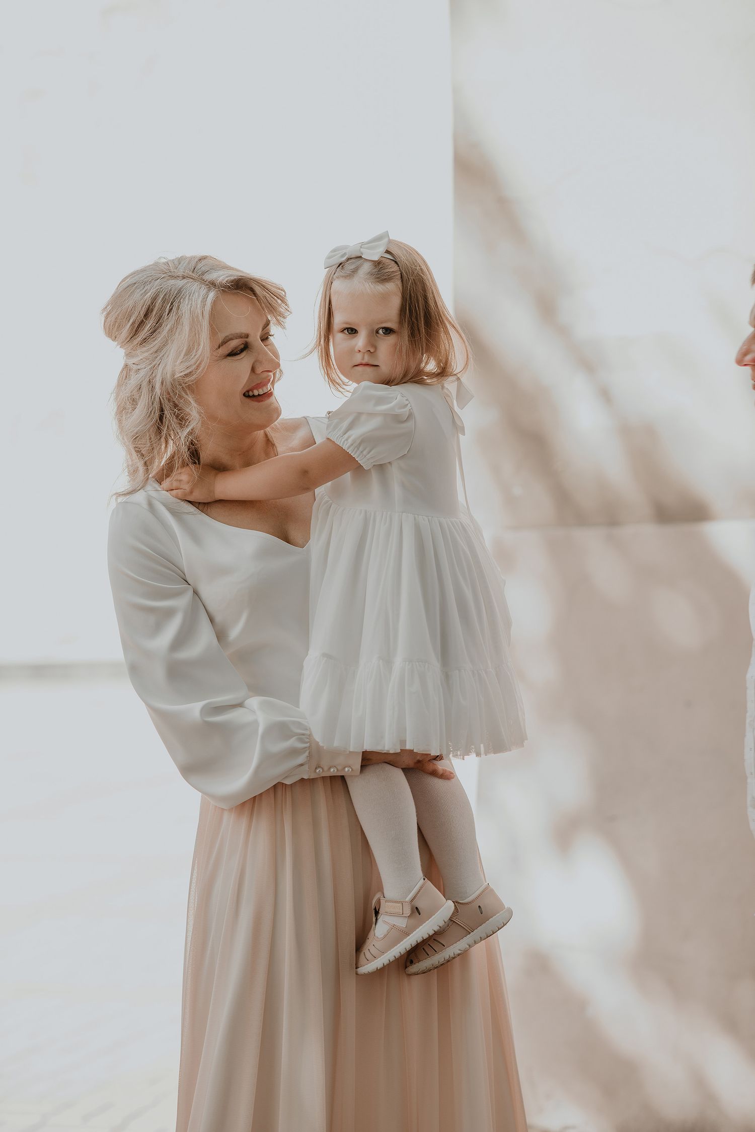 A parent and child in matching white outfits pose together against a light background in an ethereal portrait.