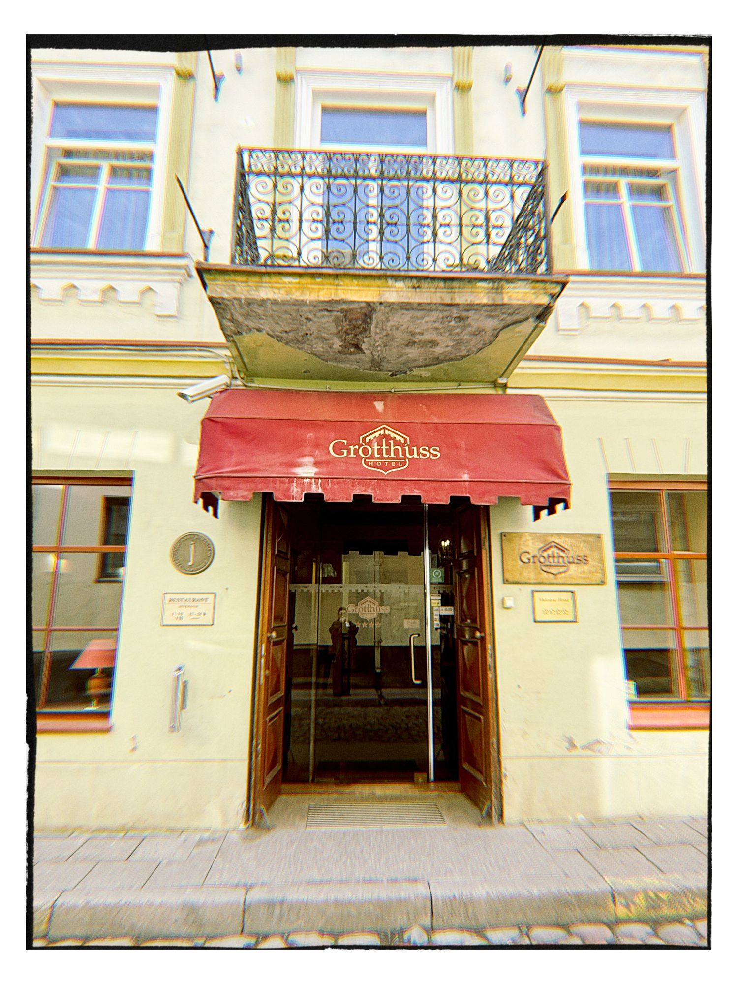 Elegant entrance of Hotel Grotthuss with red awning and ornate iron balcony in Vilnius, Lithuania.