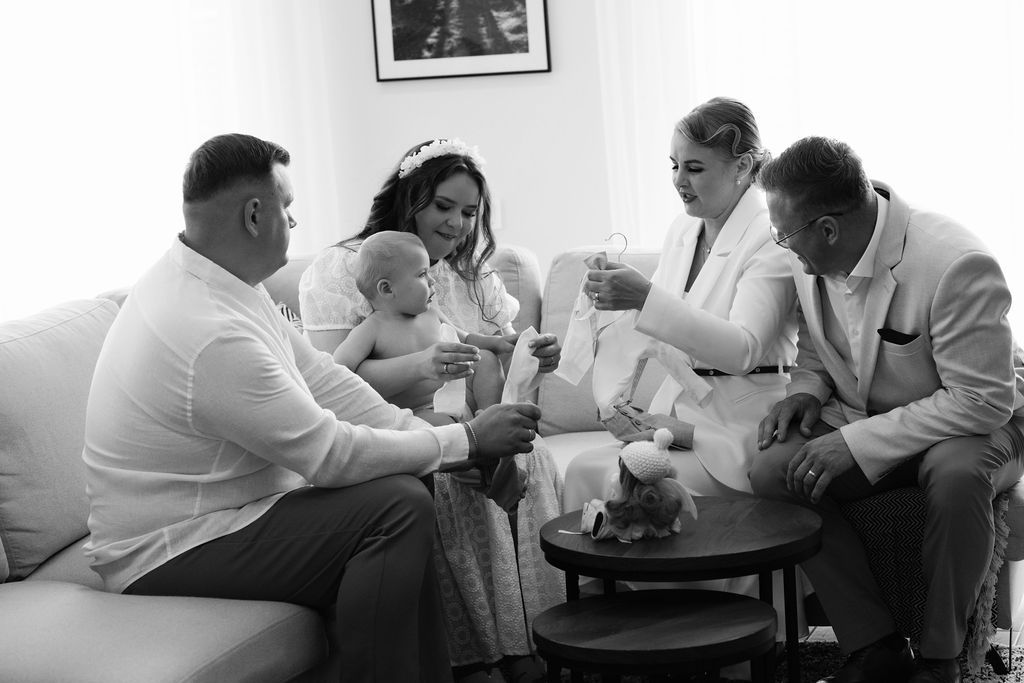Black and white photo of a family gathering on a sofa, sharing a joyful moment with a baby.