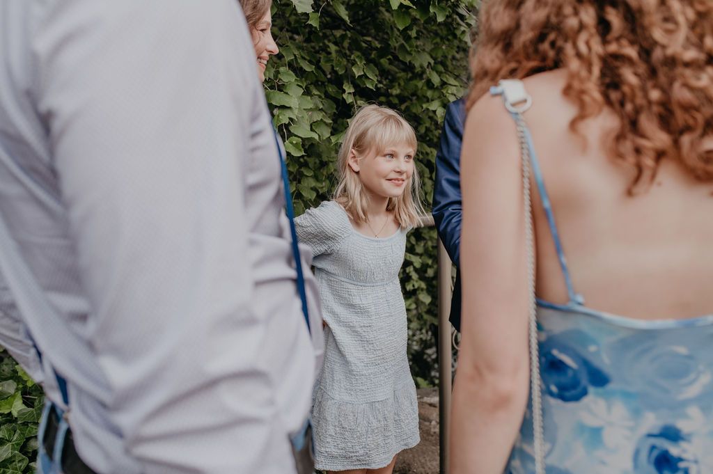 Young blonde girl in gray dress smiling at outdoor wedding celebration.
