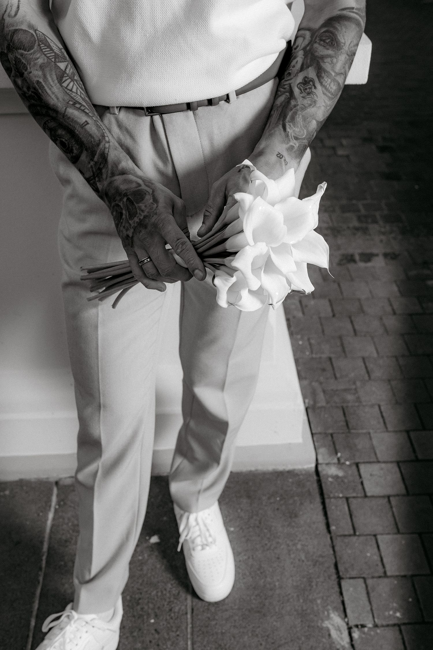 A sequence of black and white photos showing white shoes and pants with tattooed arms against a brick background.