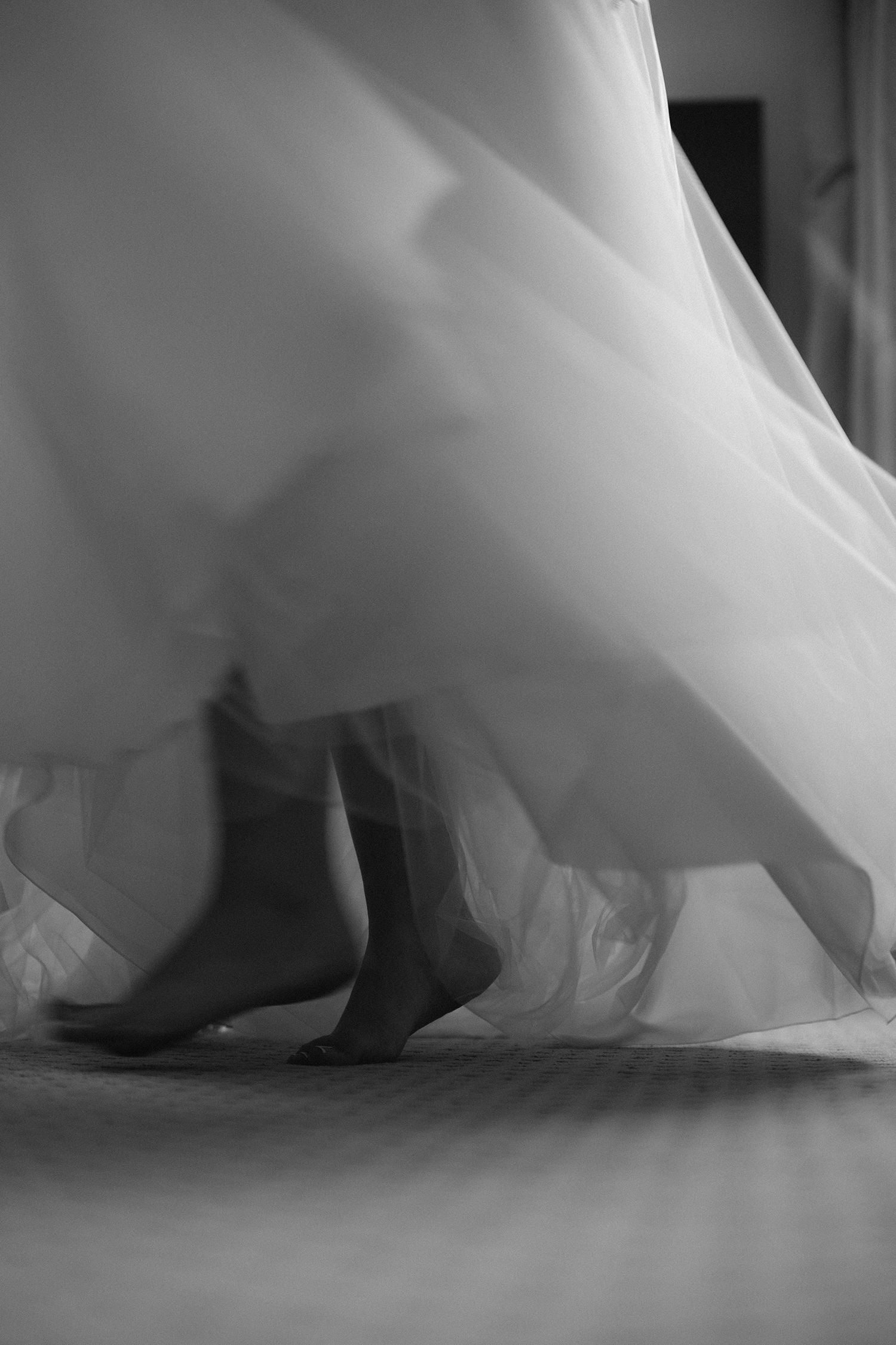 Black and white photograph of boots beneath a flowing white wedding dress, creating an elegant silhouette.