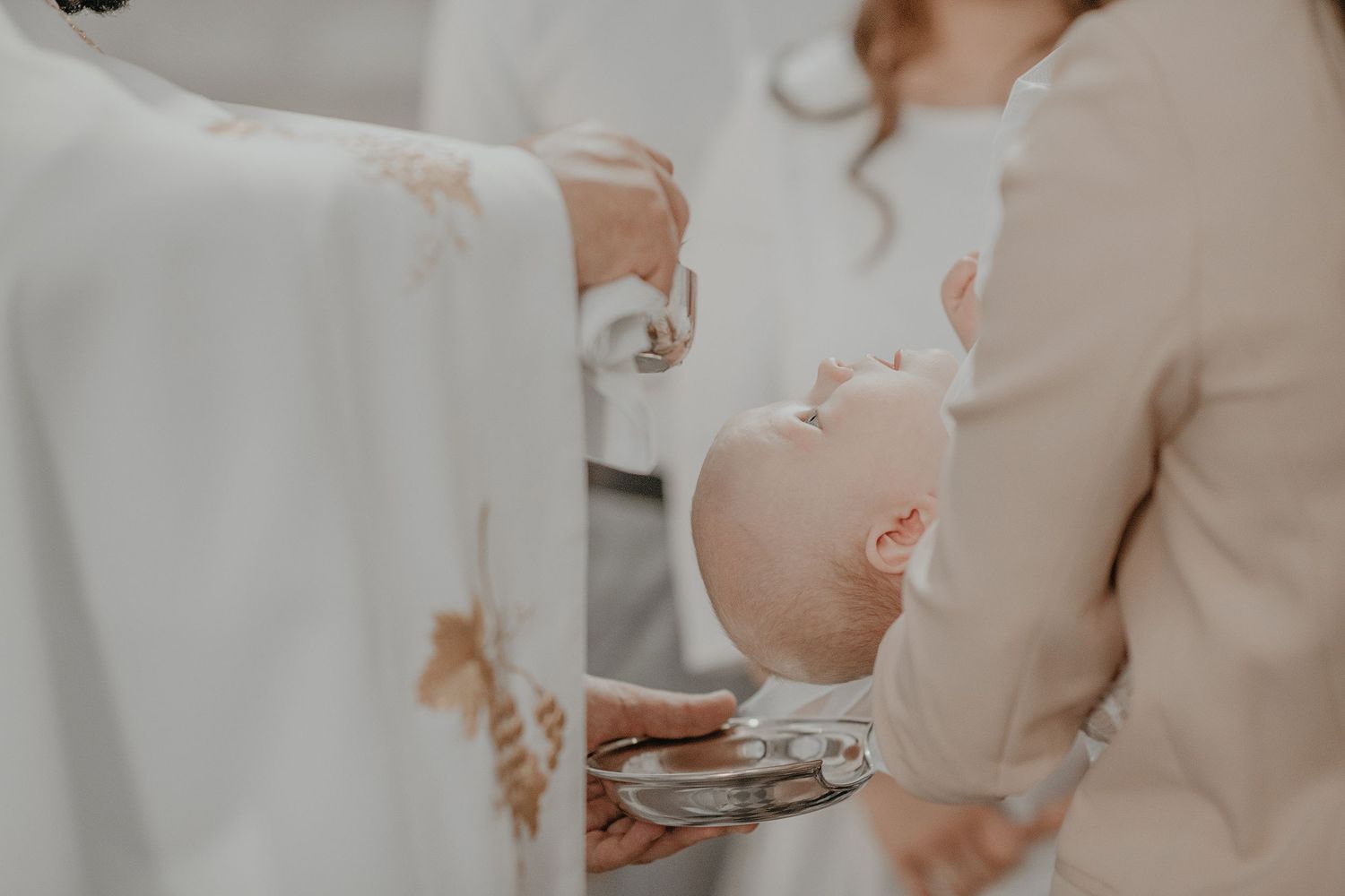 A baby in white clothing is being baptized during a religious ceremony at church.