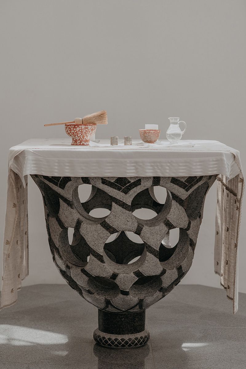 A decorative black and white vase sits beneath a white tablecloth with copper bowls and glassware on top.