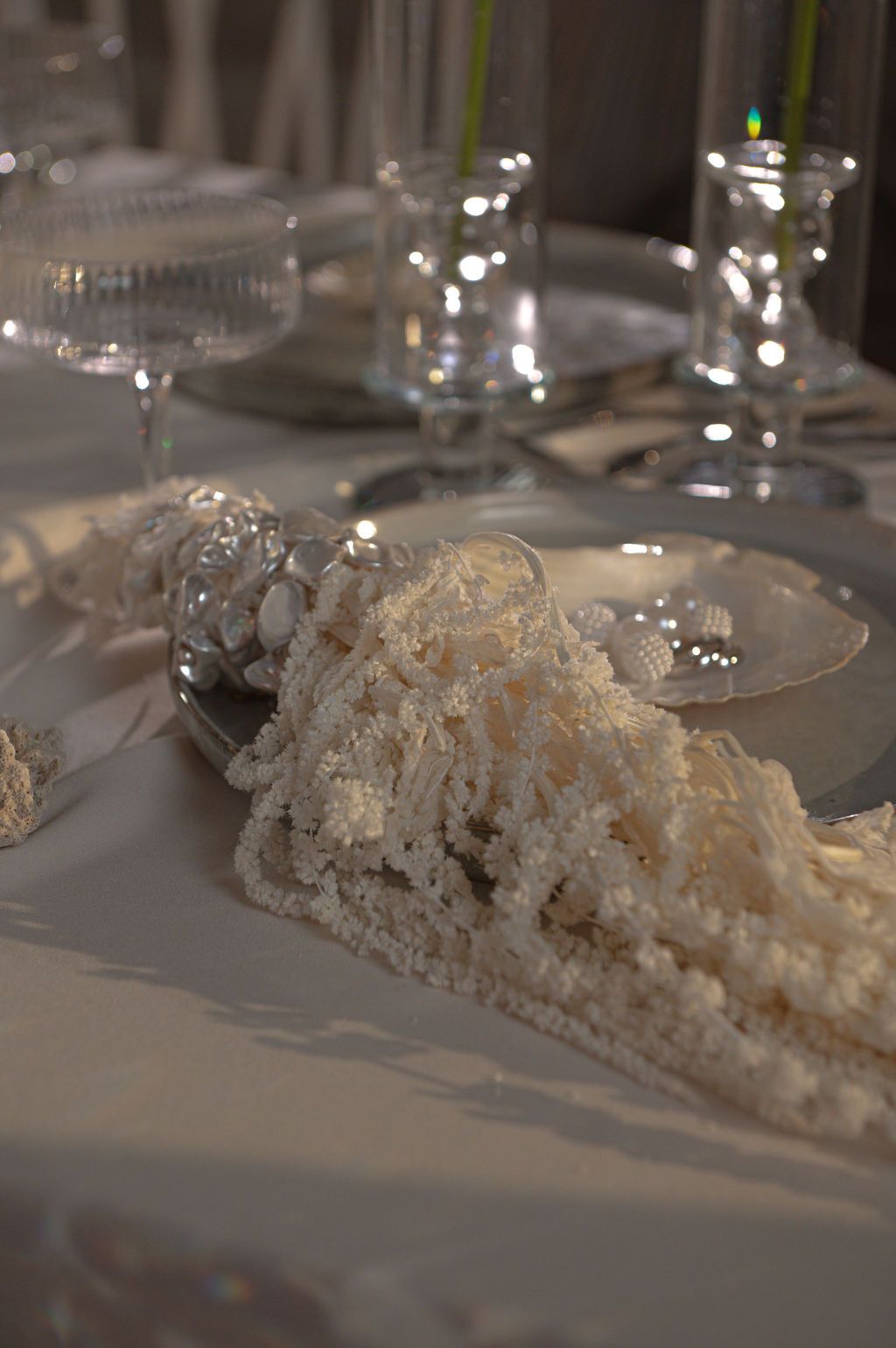 Elegant white tablescape with lace napkin, crystal glasses, and silver plates on a white tablecloth.