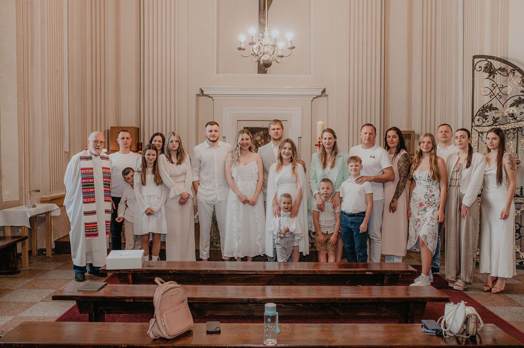 Group of people in white attire posing together in an elegant church hall during a baptism ceremony.