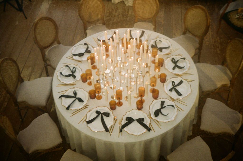 Elegant wedding reception table with tall candles, black bow napkins, and gold accents on white linen.