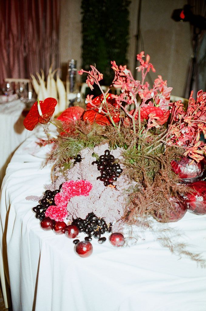 Red floral centerpiece with anthurium, berries, and wildflowers on a white tablecloth at an elegant event.