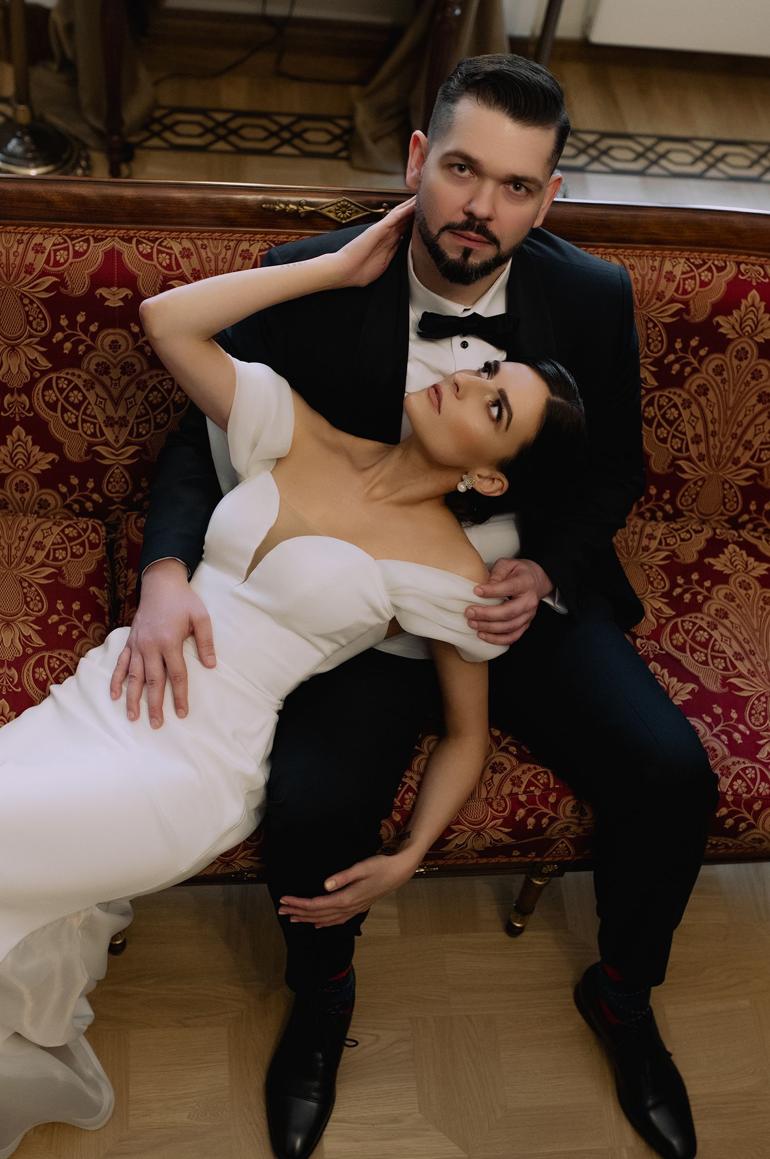 A romantic couple in formal wedding attire poses together on an elegant red and gold sofa in a sequence of intimate shots.