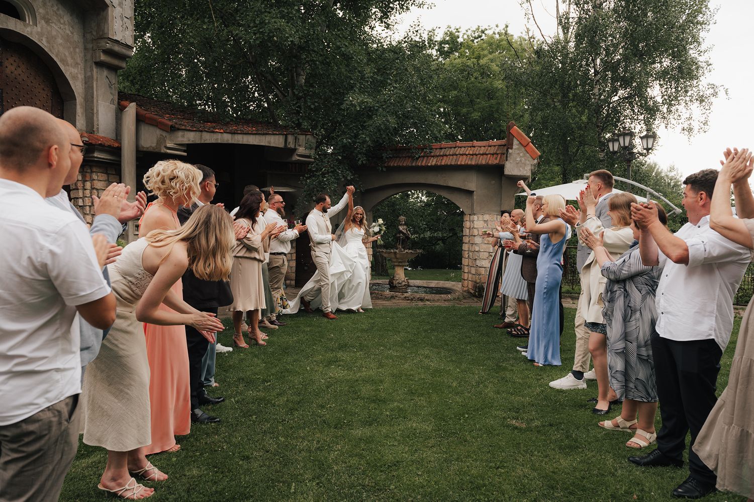 Wedding guests form a tunnel with raised arms as newlyweds walk through during an outdoor celebration.
