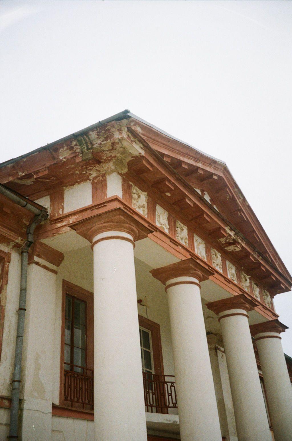 Historic neoclassical building with white columns and ornate pediment showing weathered terracotta details against overcast sky.
