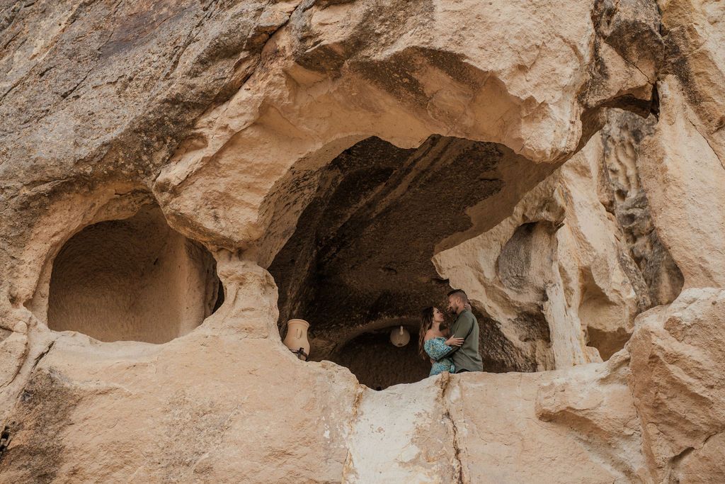 Person exploring ancient cave dwellings carved into sandstone rock formations in a desert landscape.