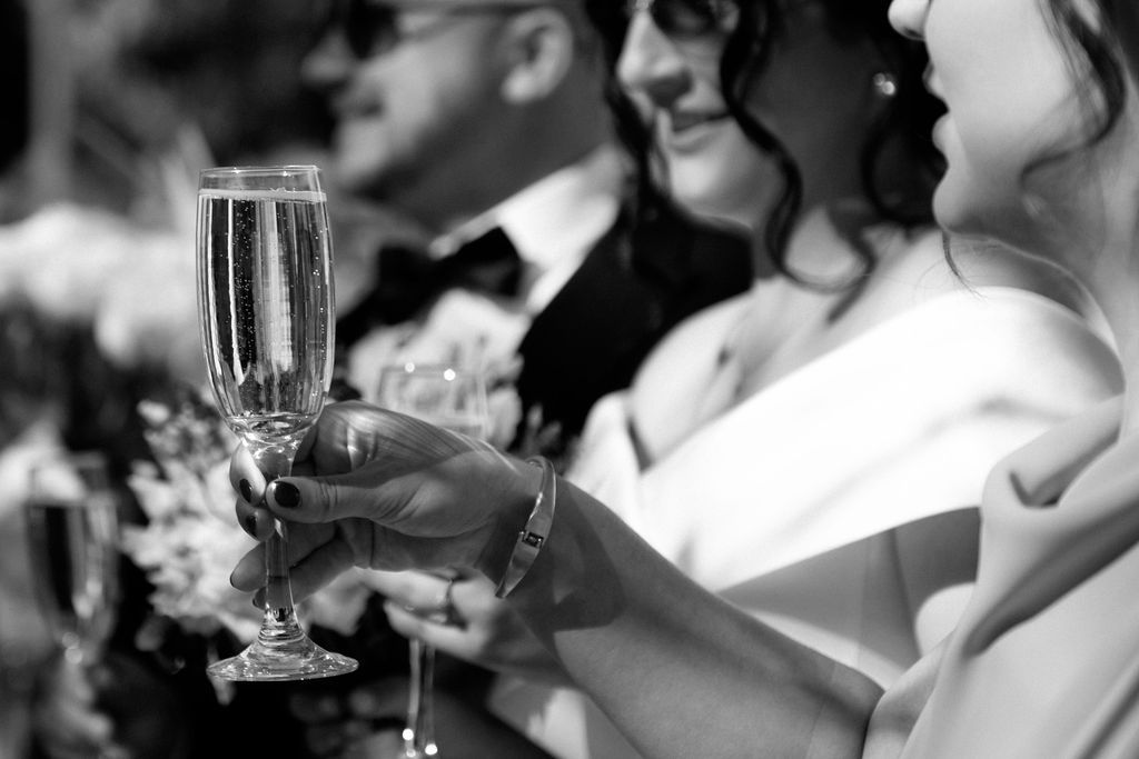 Black and white photo of wedding guests clinking champagne flutes during a celebratory toast at a reception.