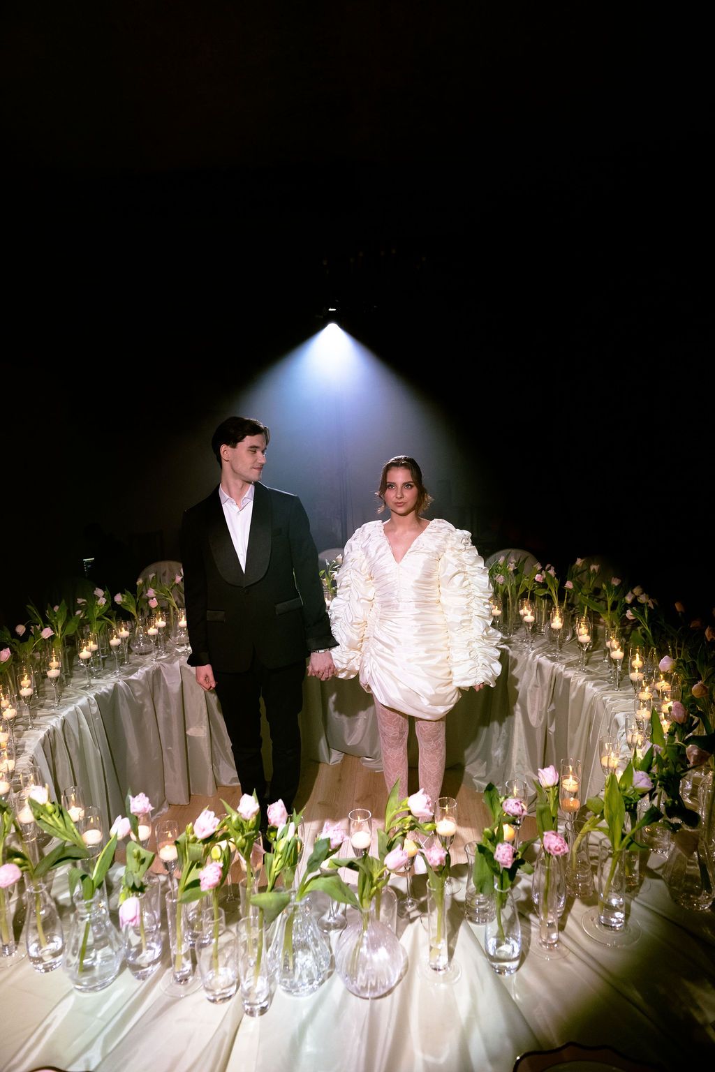 Couple in formal wear standing among pink tulips and candles at an elegant event.