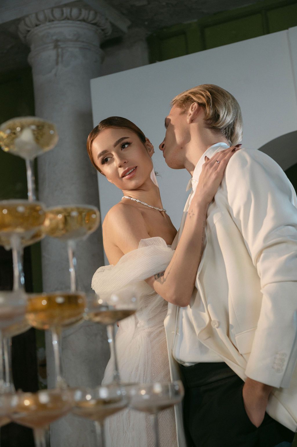 Elegant couple in formal attire sharing an intimate moment beside a champagne tower at a luxury event.