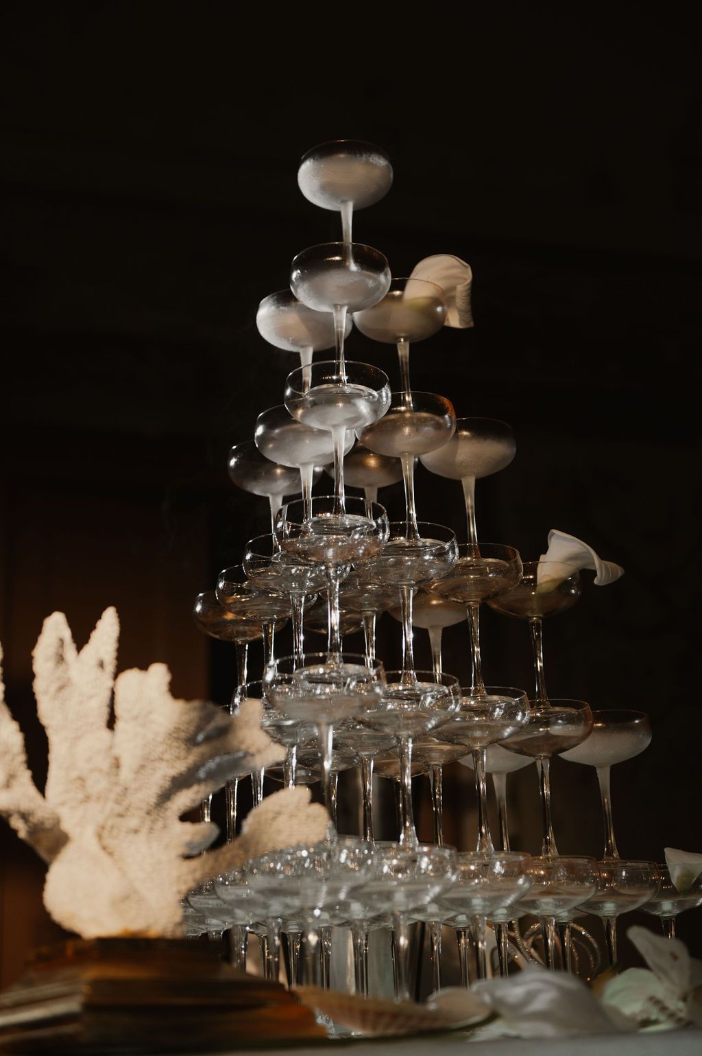 Elegant champagne tower with stacked coupe glasses and white floral decor at a formal event.