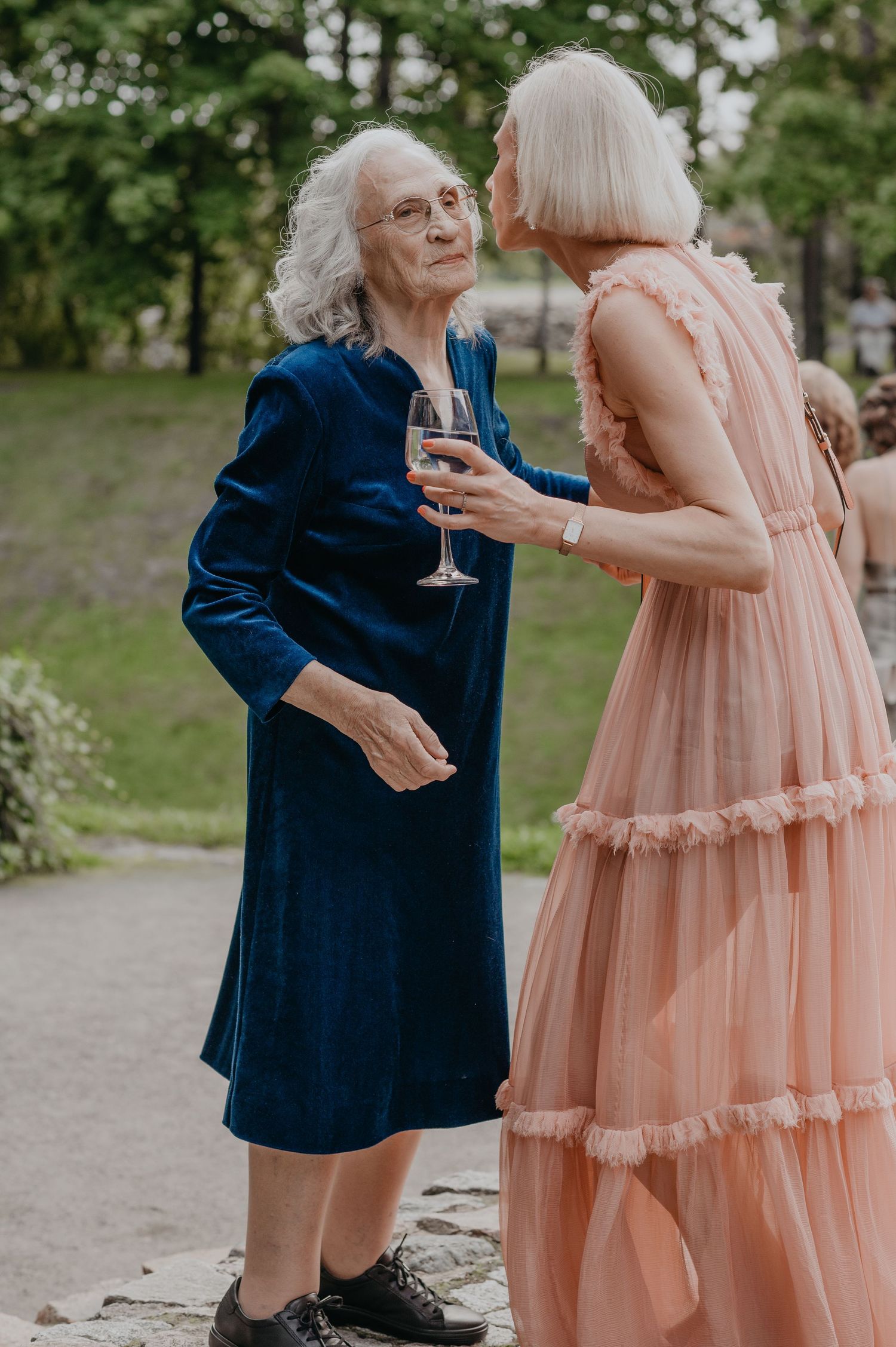 Two people in contrasting navy and peach dresses share a joyful moment at an outdoor event.