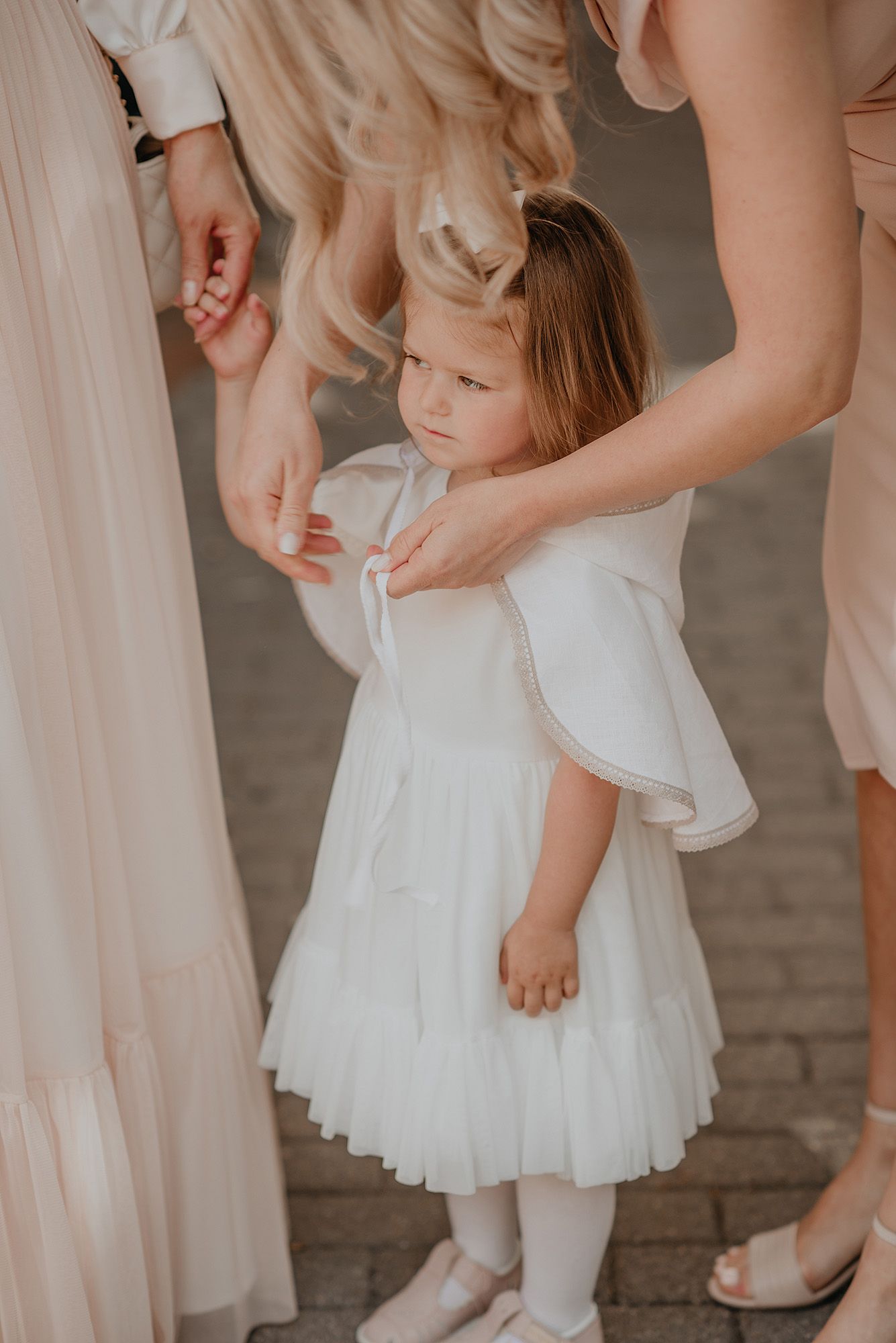 Close-up shots of a small child in a white dress with delicate details being adjusted by someone off-camera.
