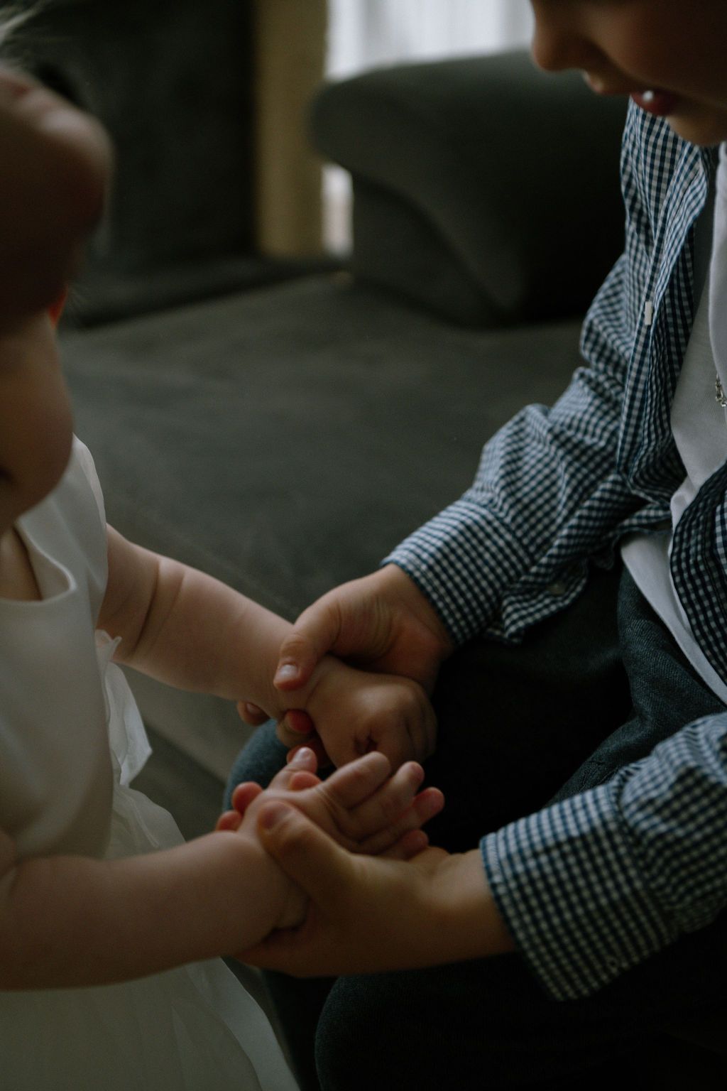 Two young children holding hands together indoors, wearing formal attire, sharing a tender moment of connection.