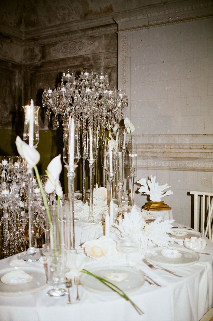 Elegant wedding reception table with crystal candelabras, white calla lilies, and fine china in a grand ornate room.