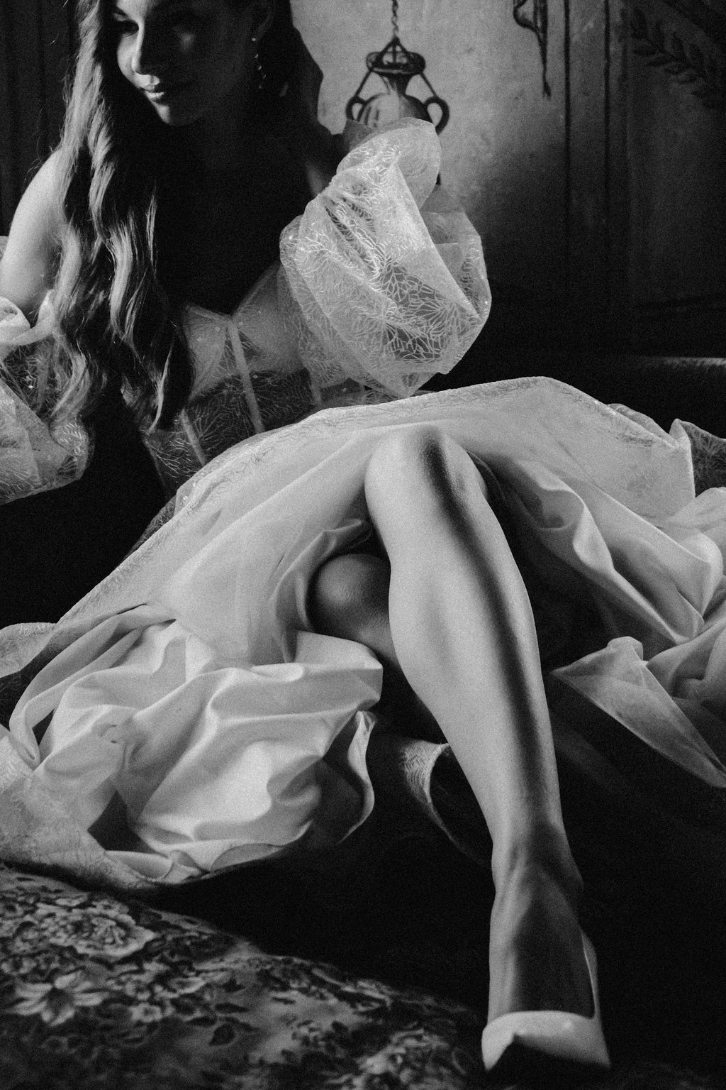Black and white photo of a woman in a flowing lace dress seated elegantly on a floral couch.