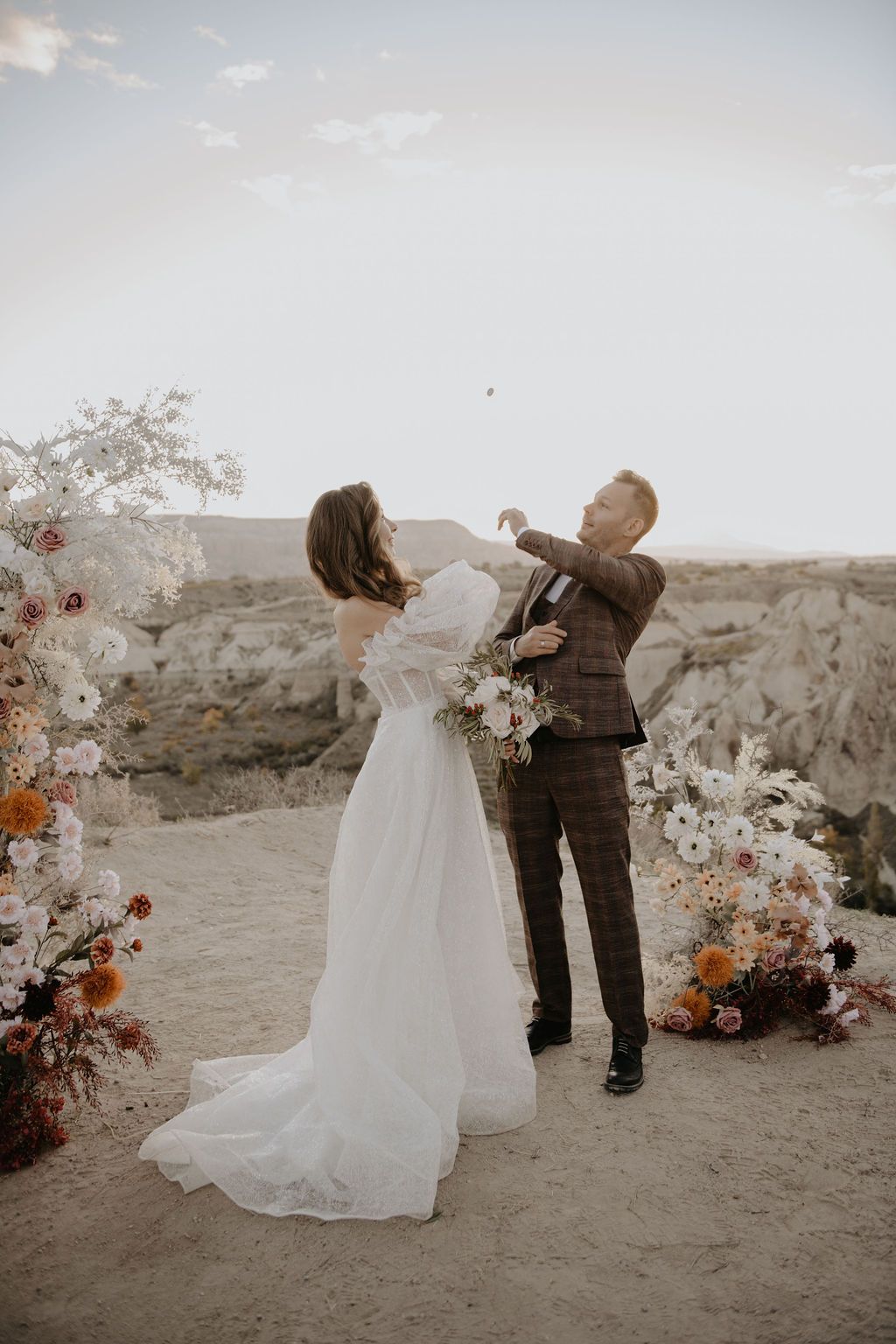 Bride and groom celebrating at outdoor desert wedding ceremony with floral arch and rocky landscape backdrop.
