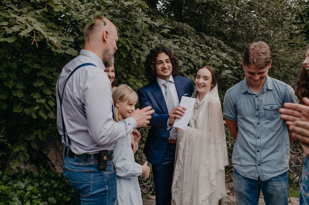 Wedding guests celebrating with bride and groom in lush garden setting.