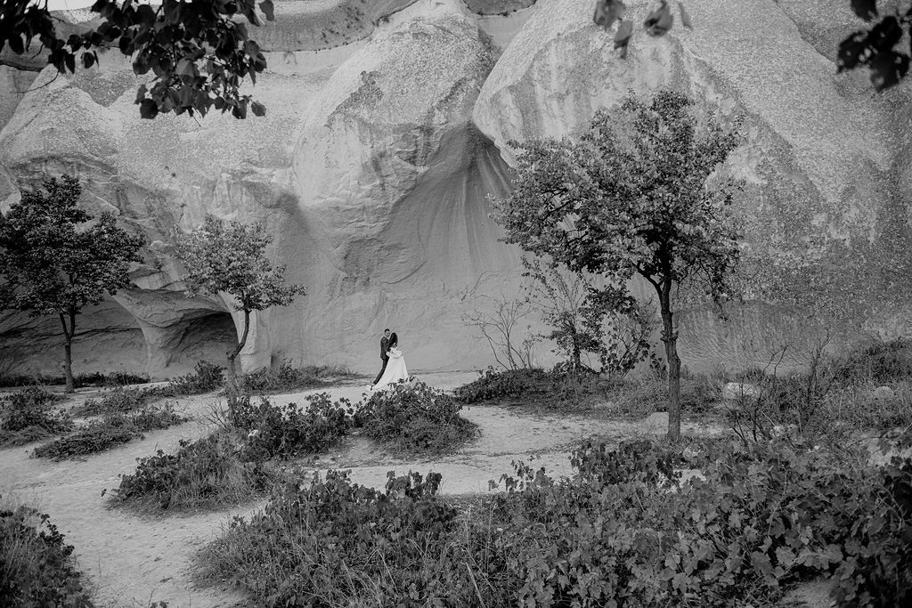Black and white photo of a wedding couple embracing among trees and rocky formations in Cappadocia, Turkey.