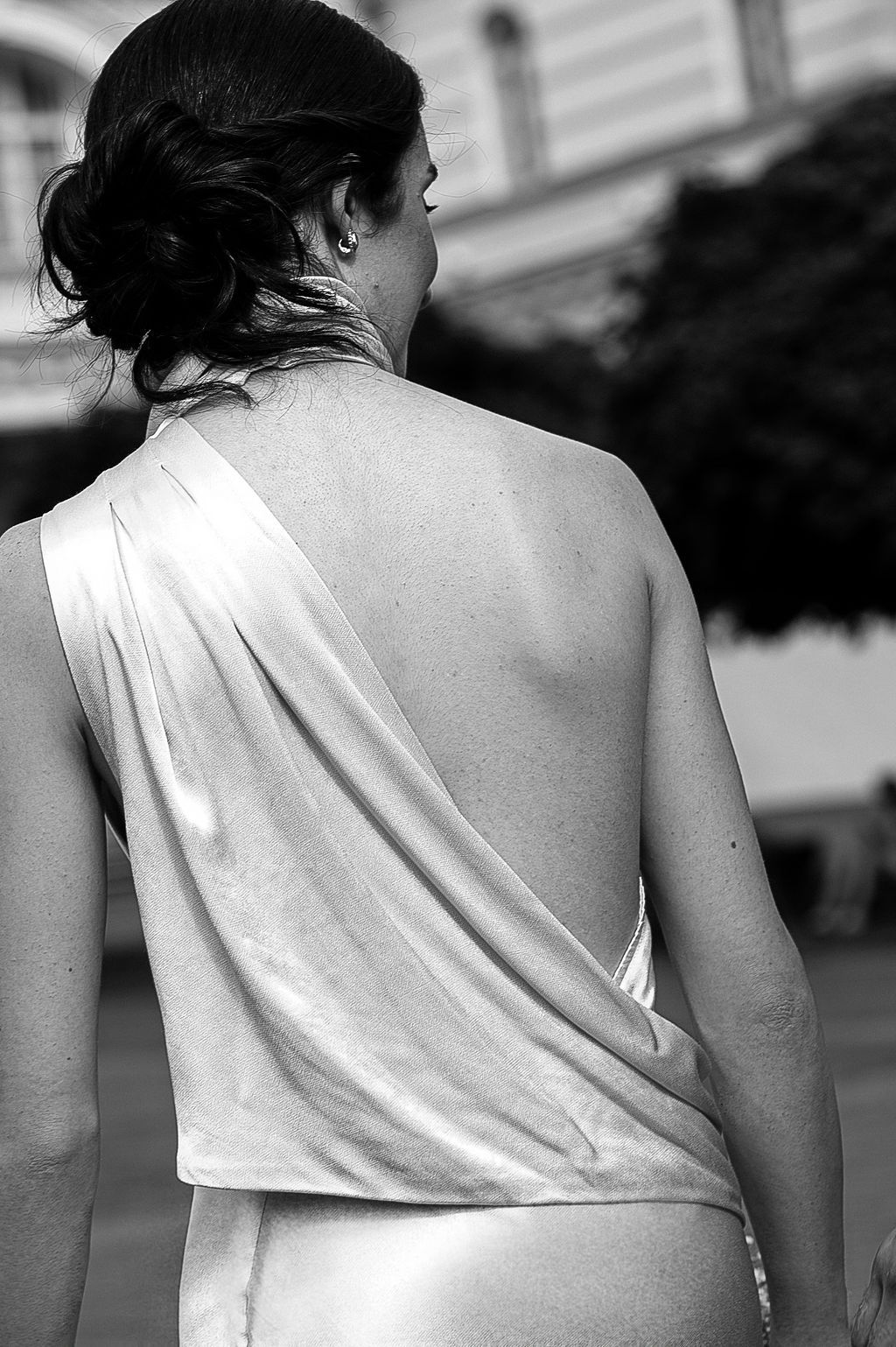 Black and white photo of a woman in an elegant backless draped satin gown, viewed from behind outdoors.