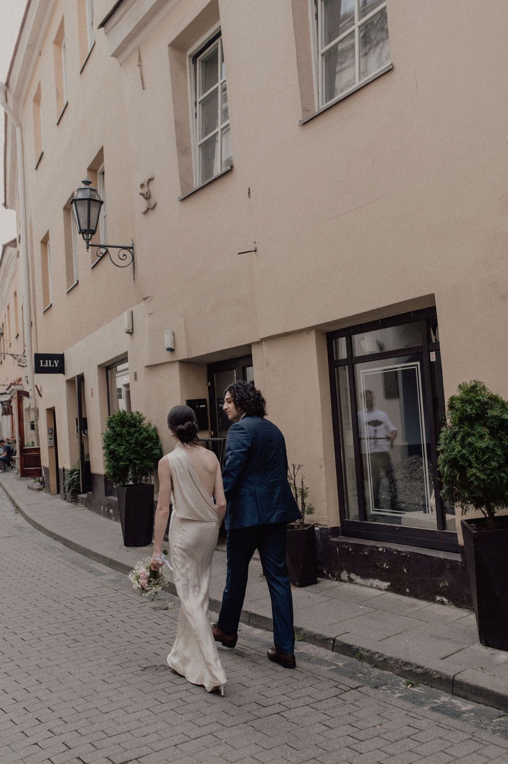 Elegant bride and groom walking hand in hand along a charming European old town cobblestone street.