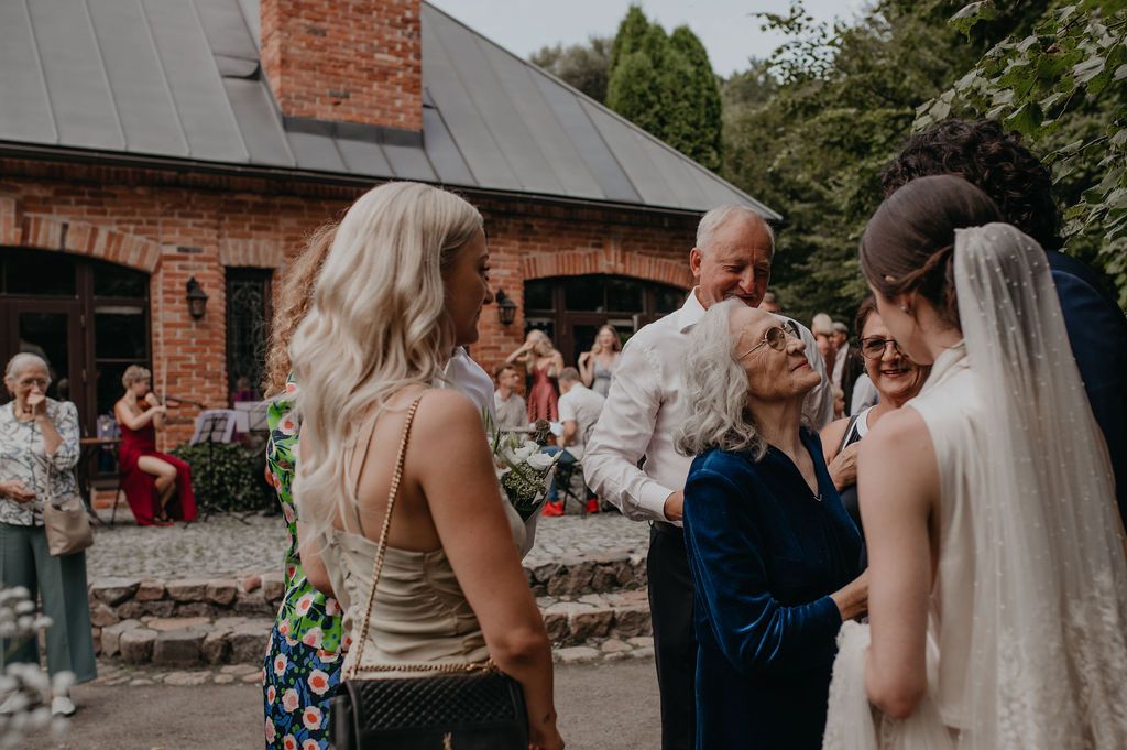 Bride in white veil receiving heartfelt congratulations from elderly guests at outdoor wedding reception.