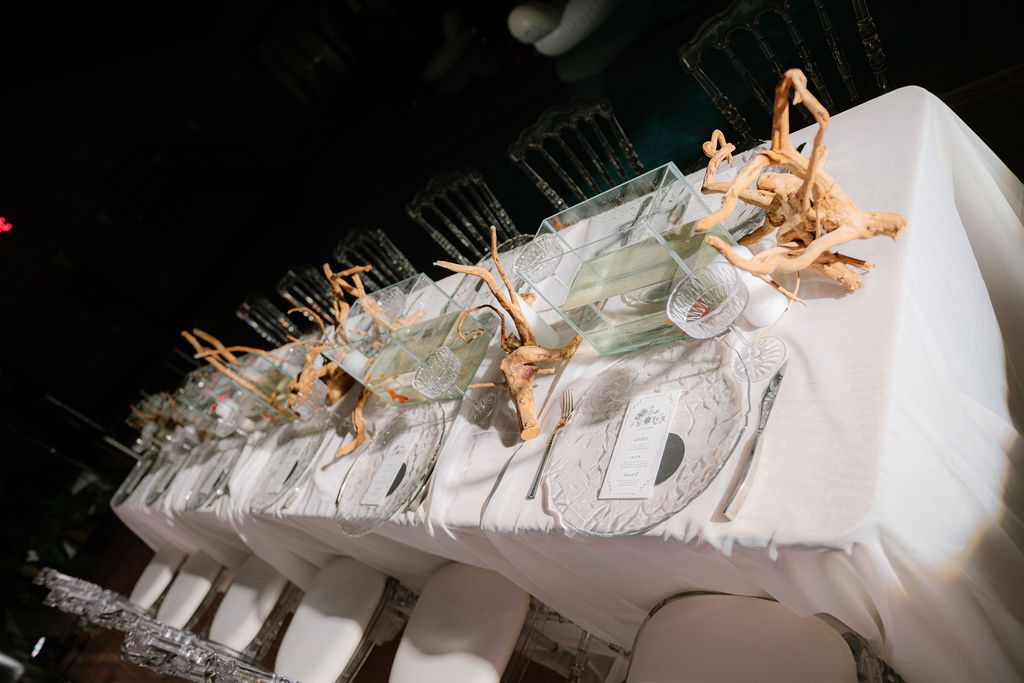 Elegant white banquet table set with crystal glassware and gold driftwood centerpieces at a formal event.