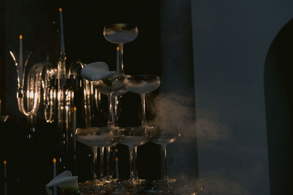 Elegant champagne tower glasses stacked in pyramid with dramatic lighting and smoke effect at upscale event.