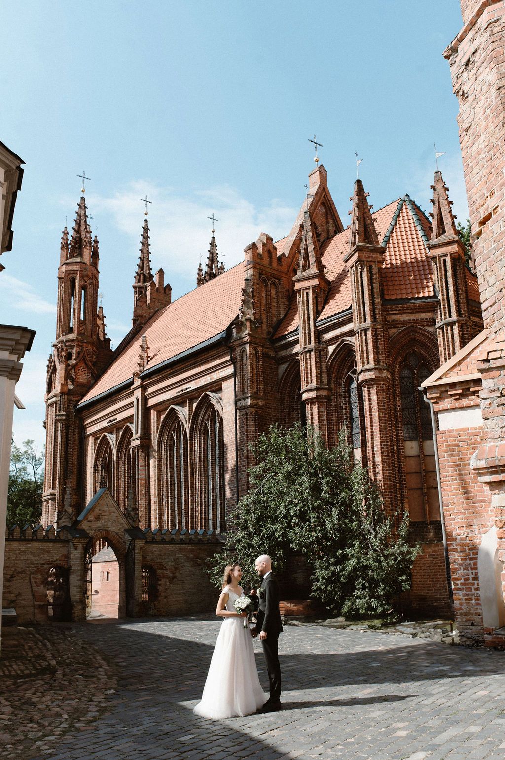 Bride and groom stand before stunning Gothic red brick St. Anne's Church in Vilnius, Lithuania on their wedding day.