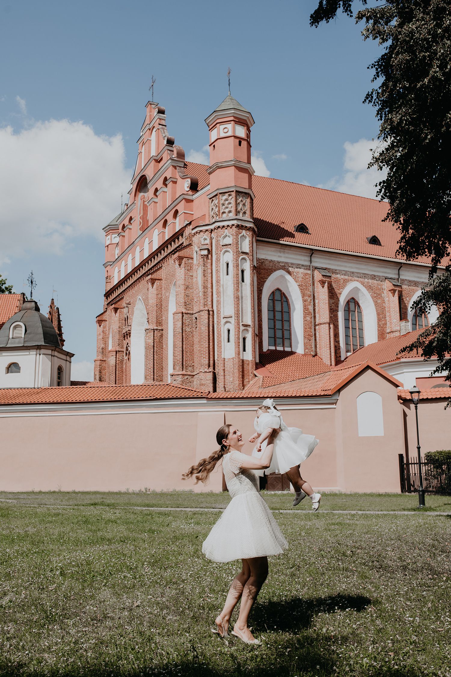 A joyful moment captured outside a pink Gothic church with a person in a white dress playing with a dog on the lawn.