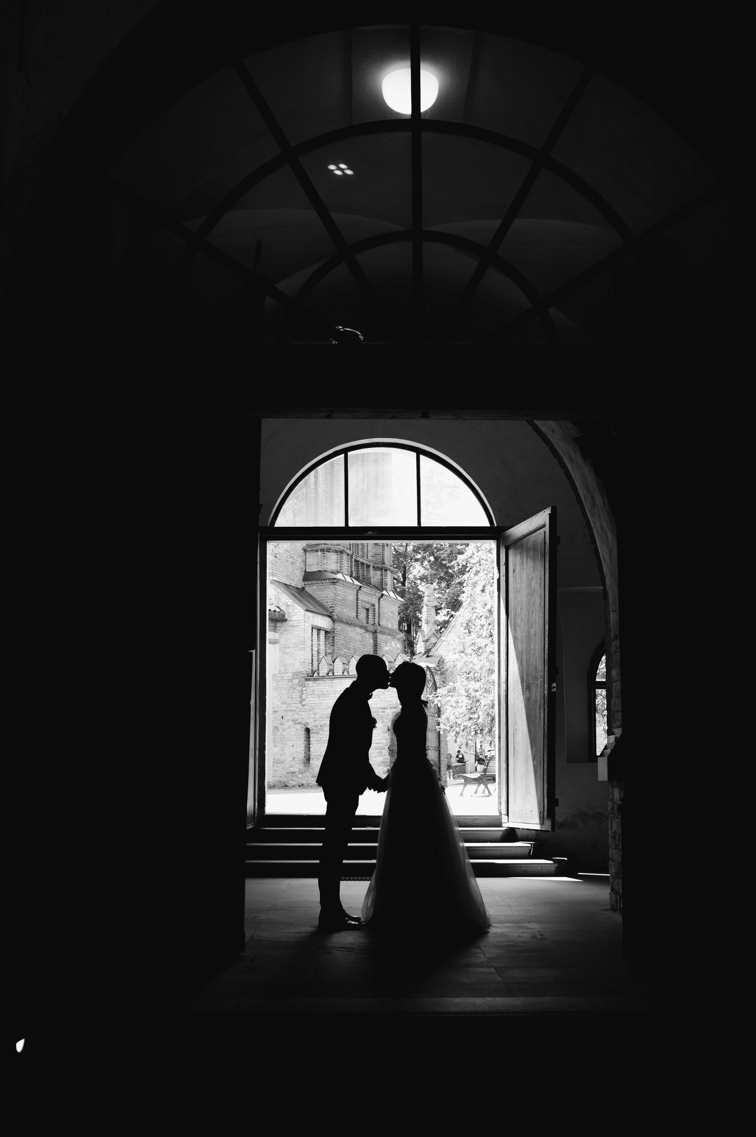 Dark silhouettes of people stand in an arched doorway or passageway creating a dramatic backlit composition.