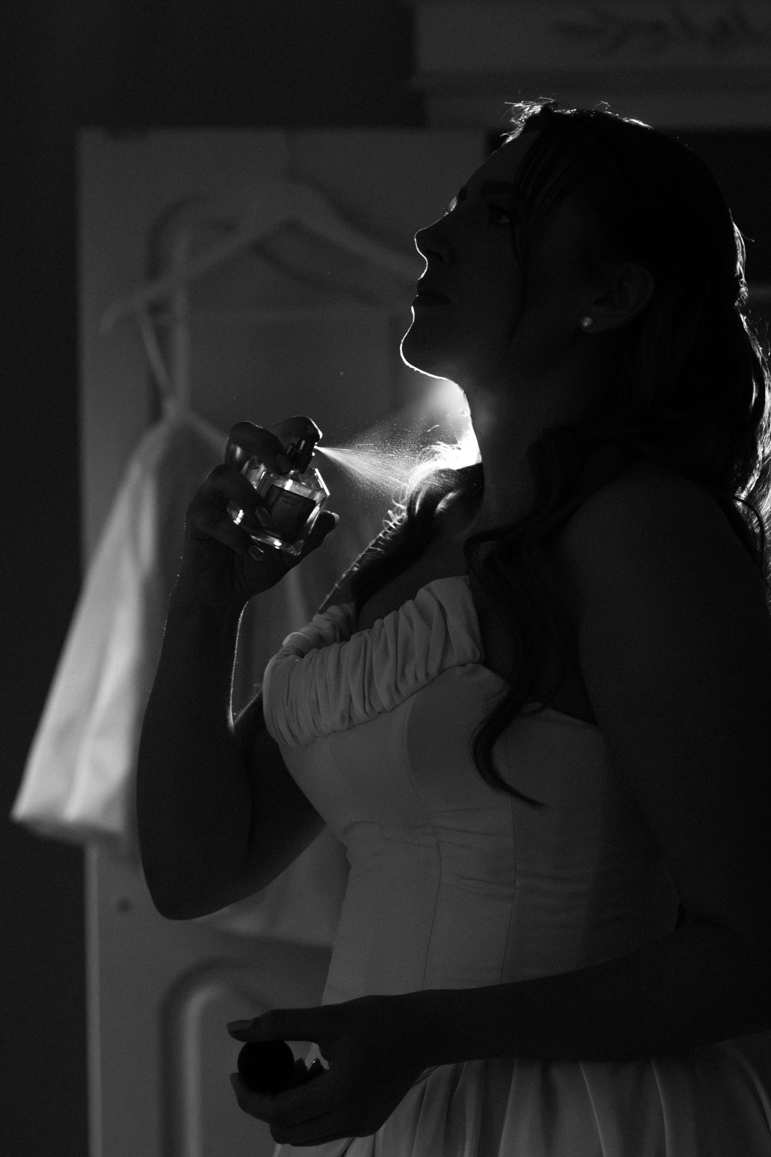 Bride in strapless wedding gown applying perfume in dramatic black and white light.