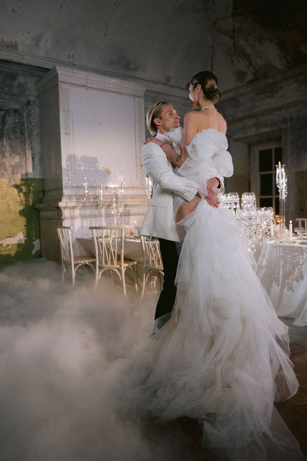Bride and groom share first dance surrounded by fog in an elegant vintage ballroom with candelabras and white decor.