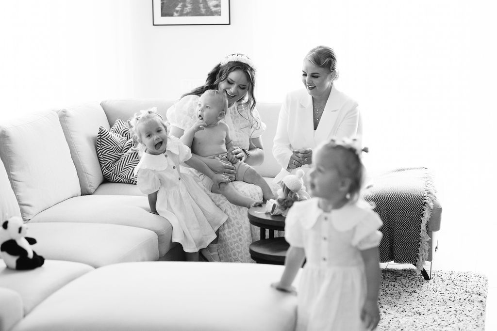 Black and white photo of two women in robes with toddlers in white dresses enjoying a relaxed morning together.