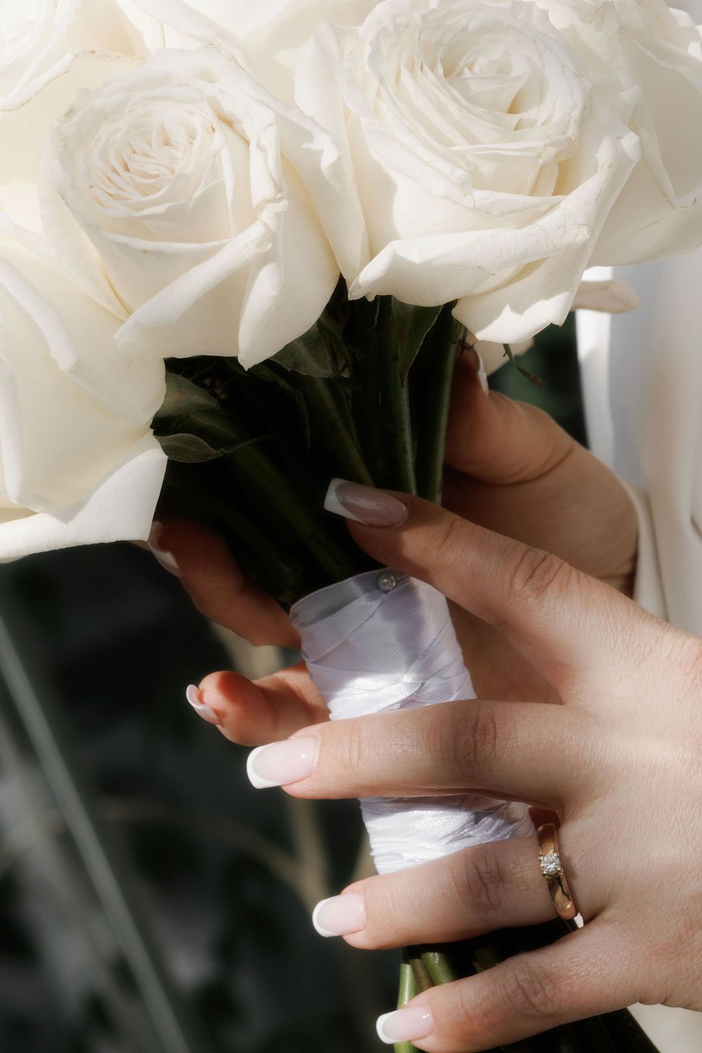 Bride holding a bouquet of white roses with a diamond engagement ring on her finger.